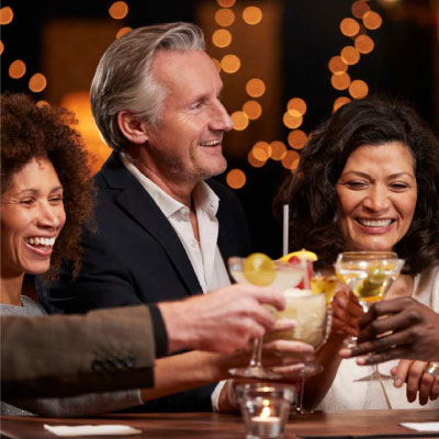 A group of three people enjoying drinks at an elegantly set table with ambient lighting in the background, representing an enjoyable night out where chauffeur services could enhance the experience.